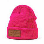 A bright pink waffle-knit beanie hat with a brown leather patch on the front cuff reading 'LITTLE BUCK'.